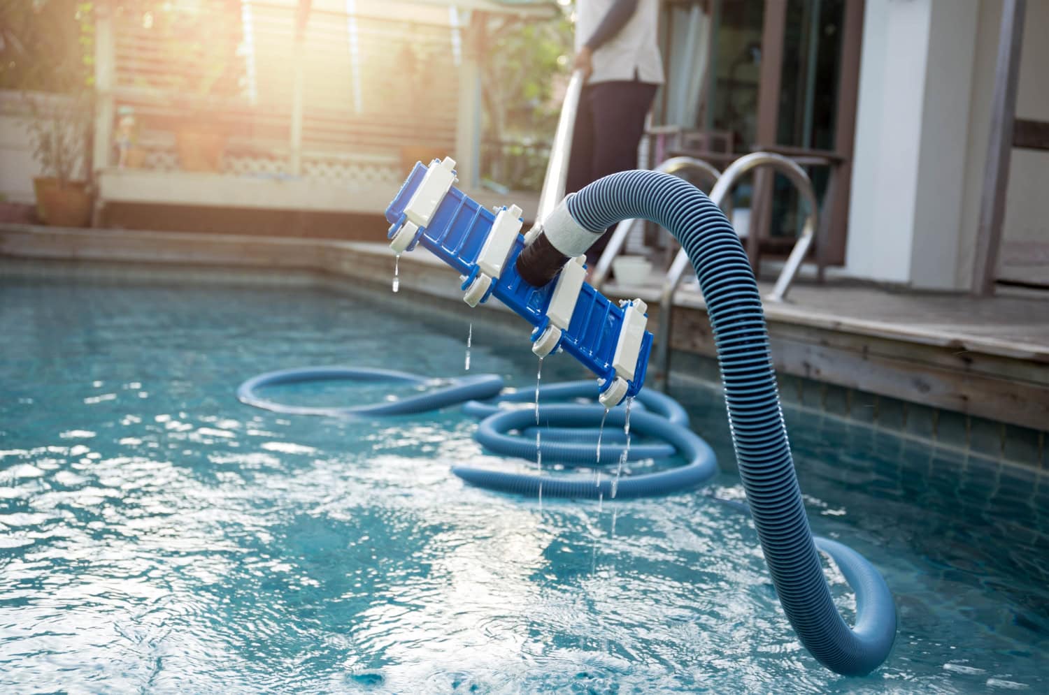 A person practices DIY pool care using a pool vacuum with a blue hose to clean a residential swimming pool near their Corpus Christi home.