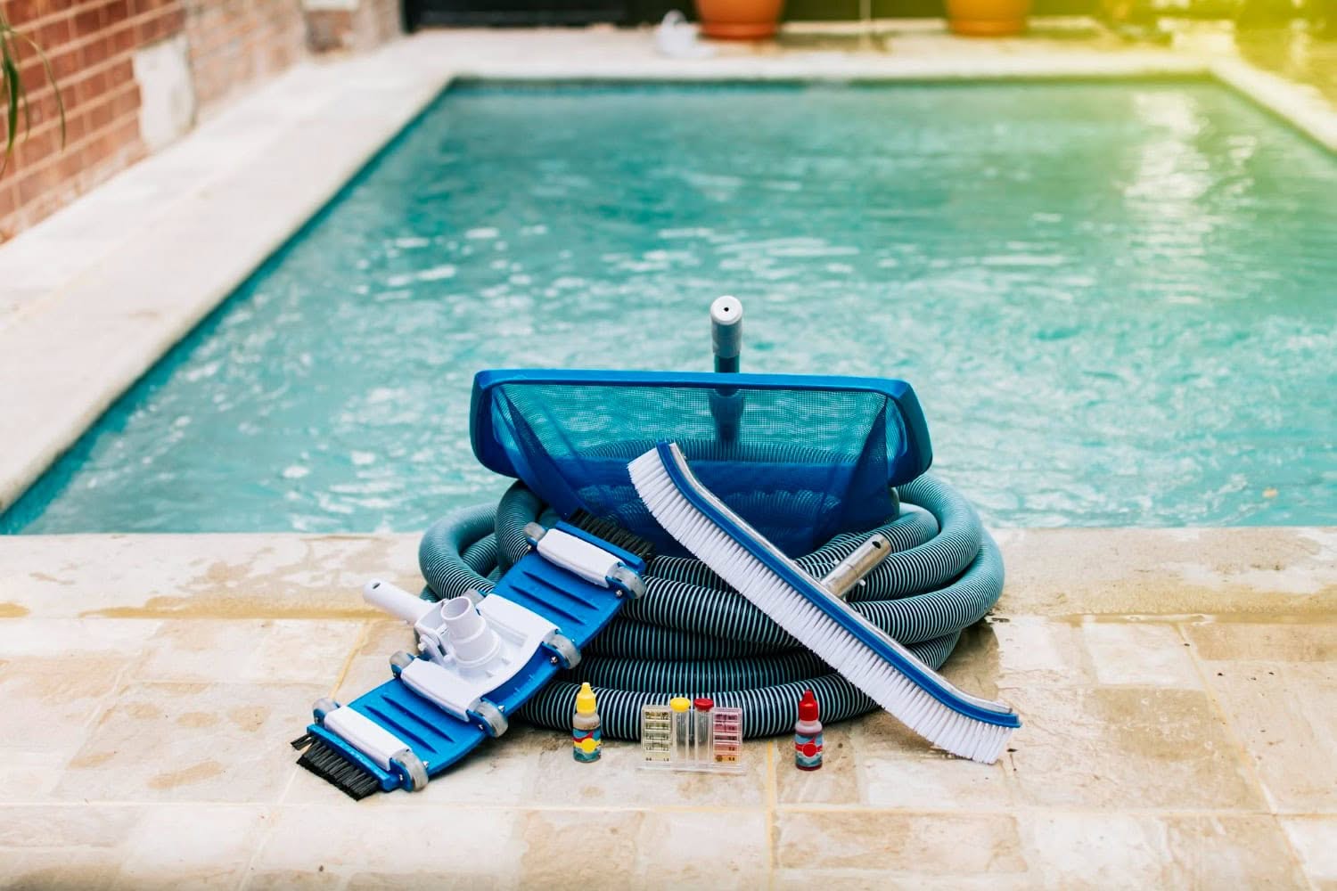 Pool cleaning equipment for maintenance, including a hose, brush, net, vacuum head, and water test kits, is arranged on the poolside next to a saltwater pool in Corpus Christi.